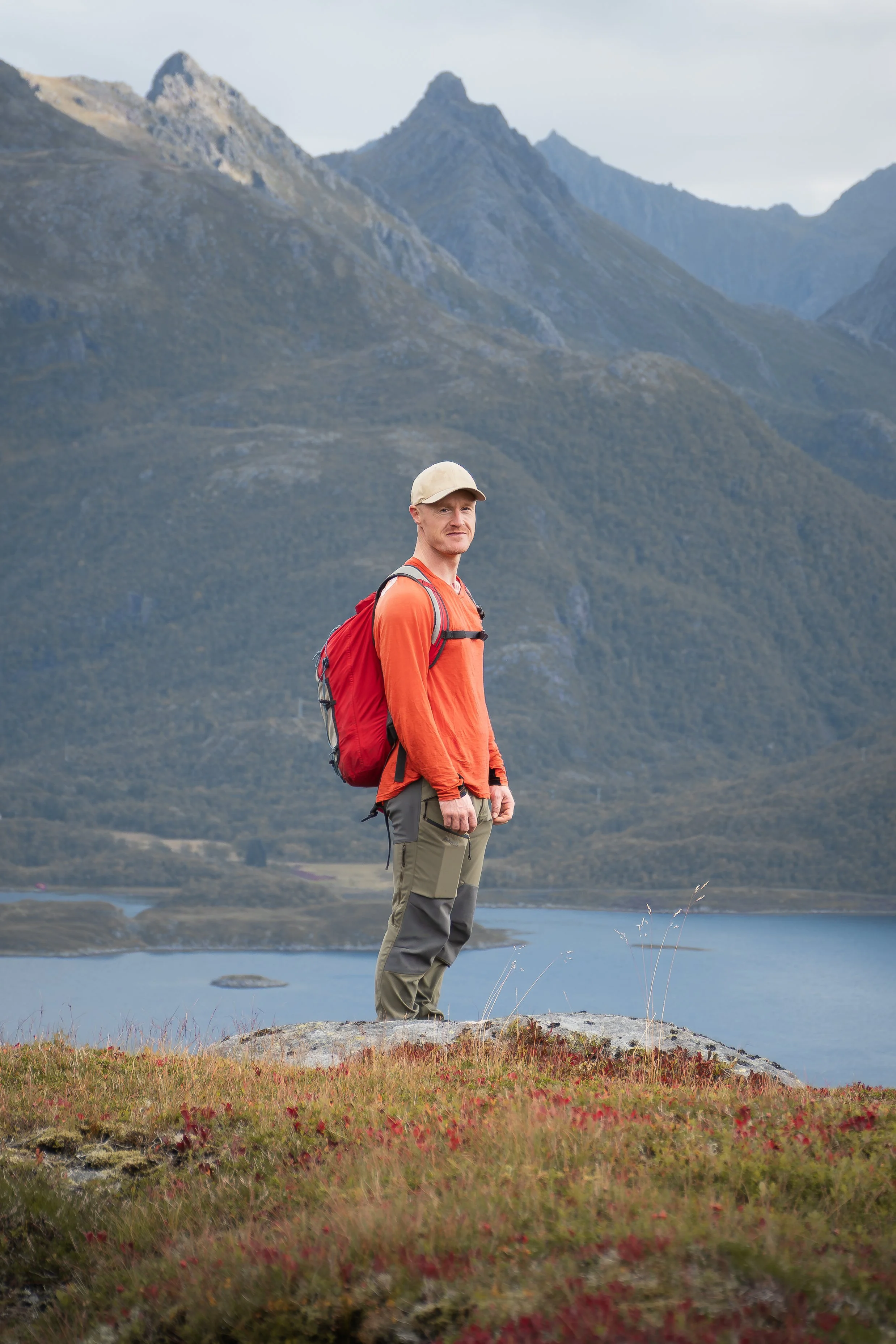 Man standing on a hill with mountains in the background and fjord underneath in western Vesterålen