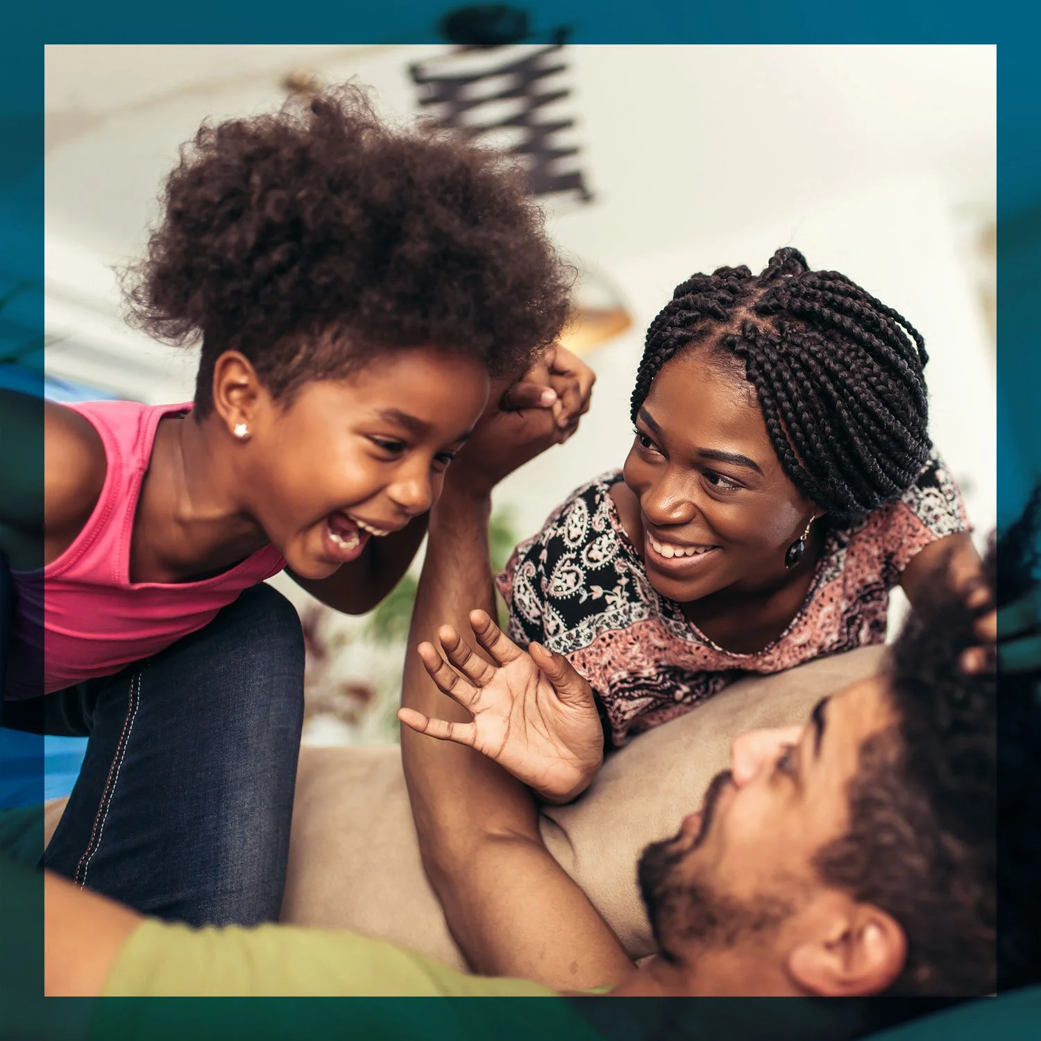 A group of diverse people, including a young girl, a woman, and others, engaging in a joyful conversation or activity indoors. The girl is smiling and leaning towards the woman, who is also smiling warmly.