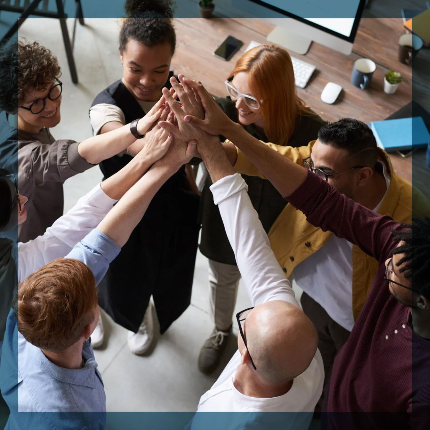 Group of diverse people putting their hands together in a team huddle in an office setting.