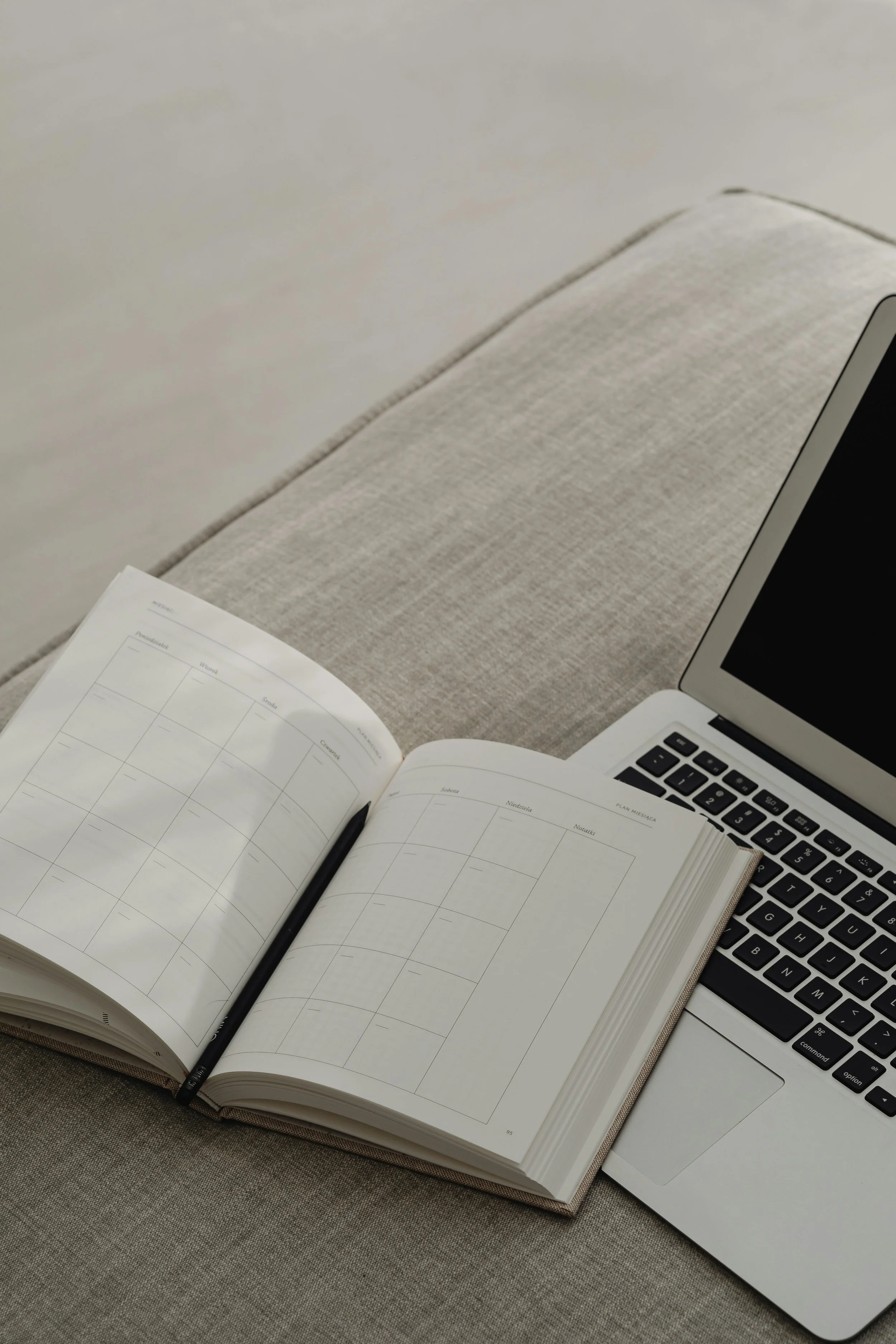 Open planner or notebook with a pen on a table, laptop partially visible, and paper with a calendar layout.