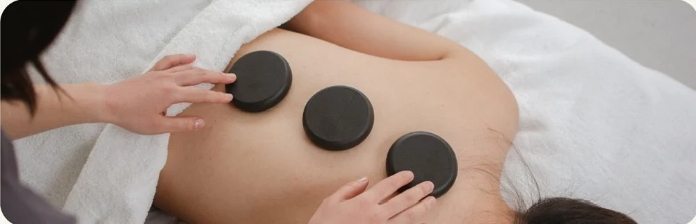 Person receiving a hot stone massage on their back with three black stones placed on their back.