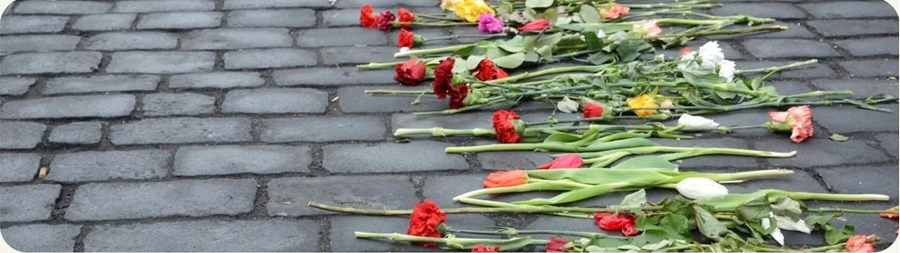 Flowers, including carnations and tulips, laid on a cobblestone street.