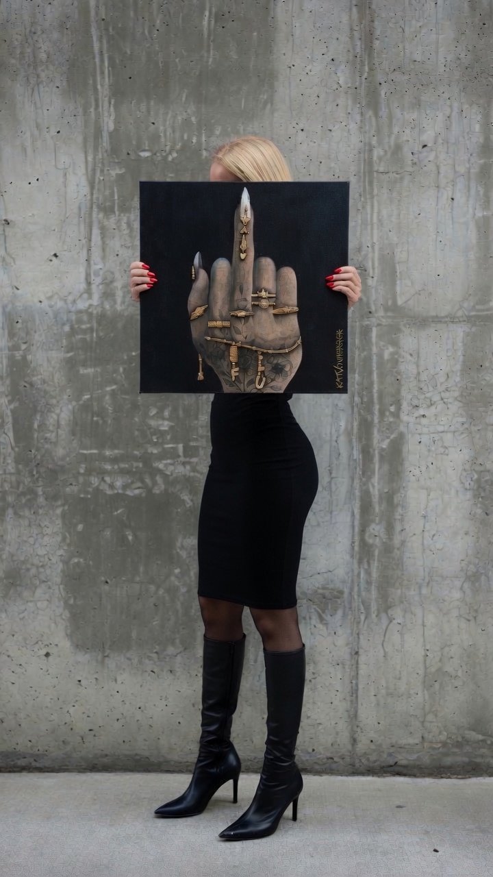 Kat von Horror holding her acrylic painting "F*** U" in front of a concrete wall.