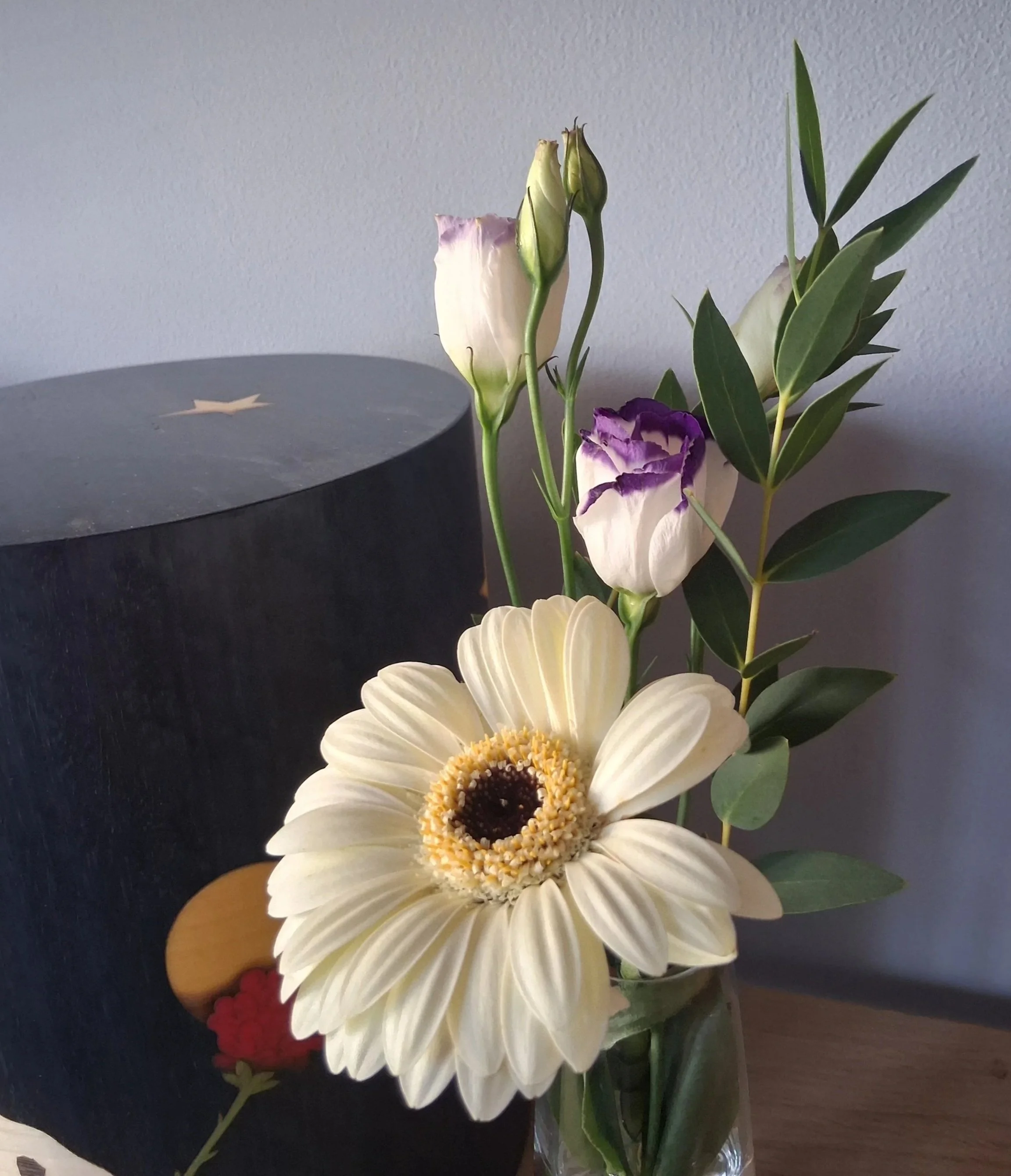 Blumenstrauß mit weißen, violetten und grünen Blumen und Blättern in einer Glasschale, auf einem dunklen Tisch