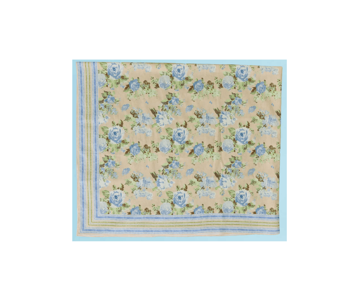 A floral patterned tablecloth with blue roses, green leaves, and cream background, bordered by a striped blue and yellow edge.