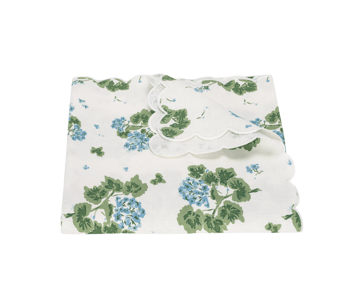 Stacked white fabric with green leaves and blue flowers pattern, and a white scalloped trim.