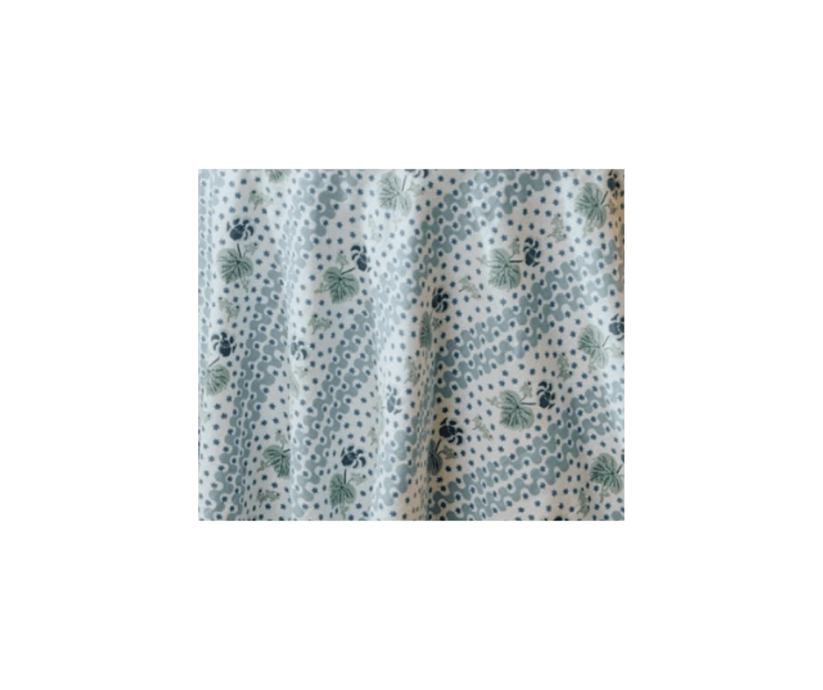 Close-up of fabric with a pattern of green leaves, small blue dots, and wavy lines on a white background.