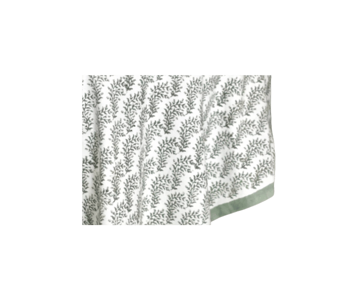 A table with a white tablecloth featuring a gray leafy pattern and green border.
