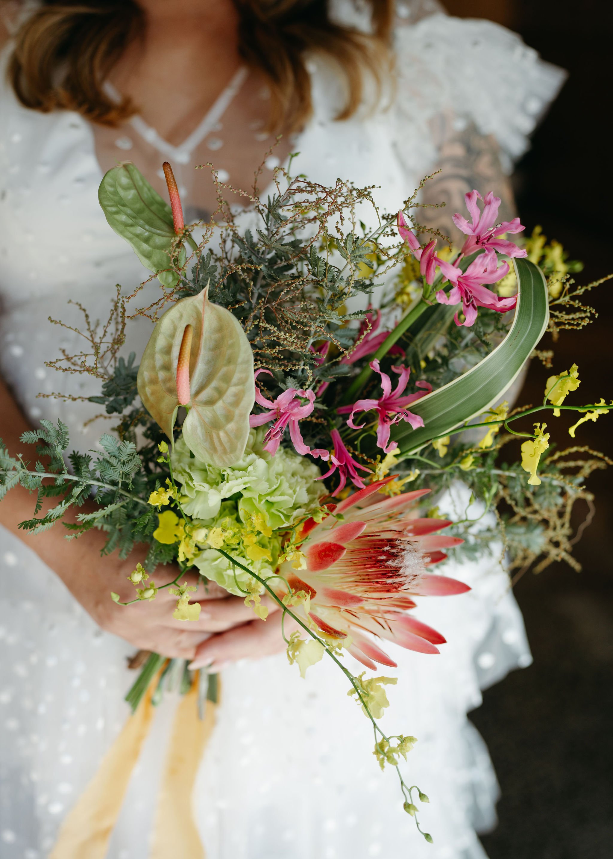 Close-up of a woman wearing a white lace dress holding a large bouquet of colorful flowers and greenery.