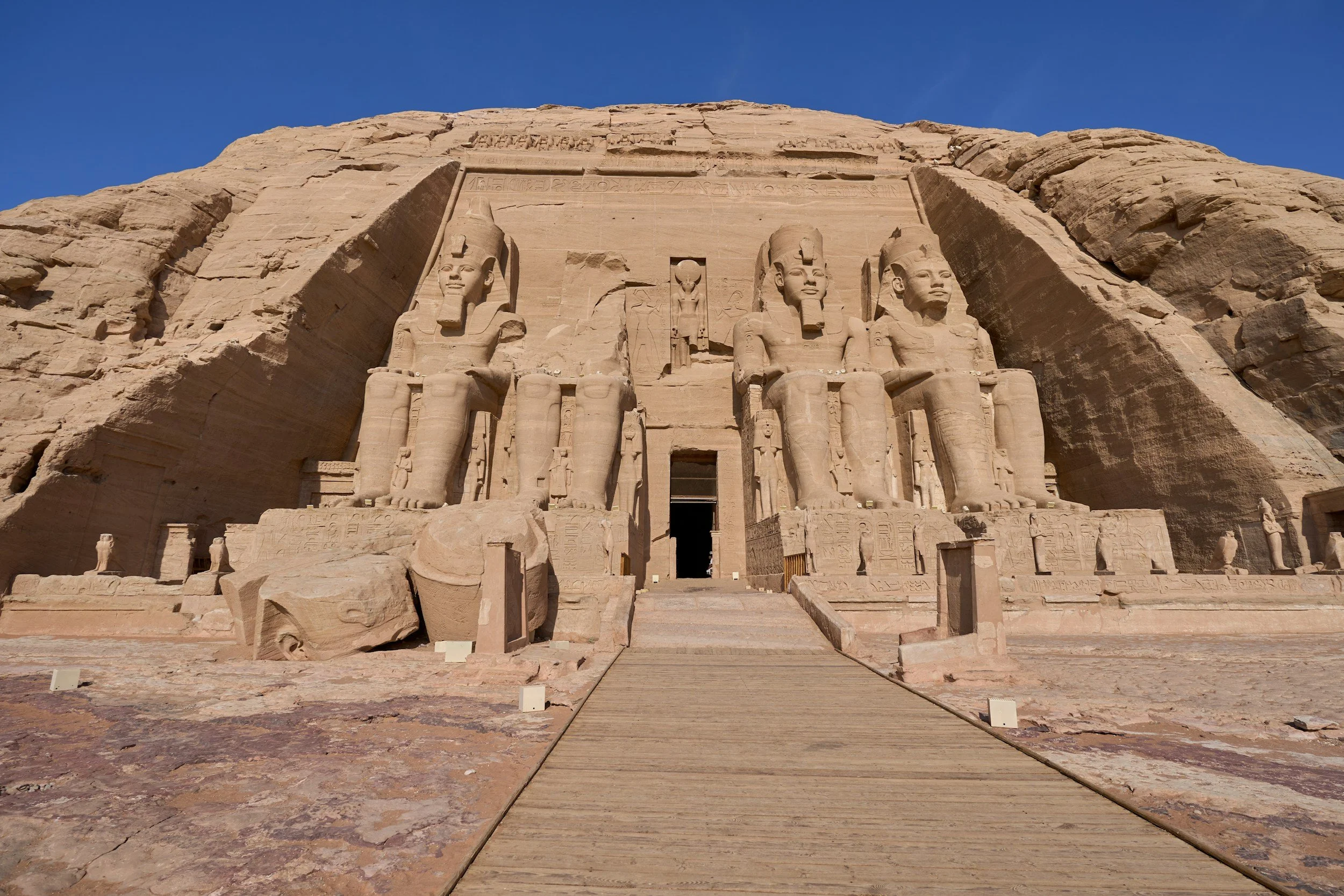 The Great Temple of Abu Simbel, an ancient Egyptian monument, with four colossal statues of Pharaoh Ramses II at the entrance, carved into a sandstone mountain under a clear blue sky.