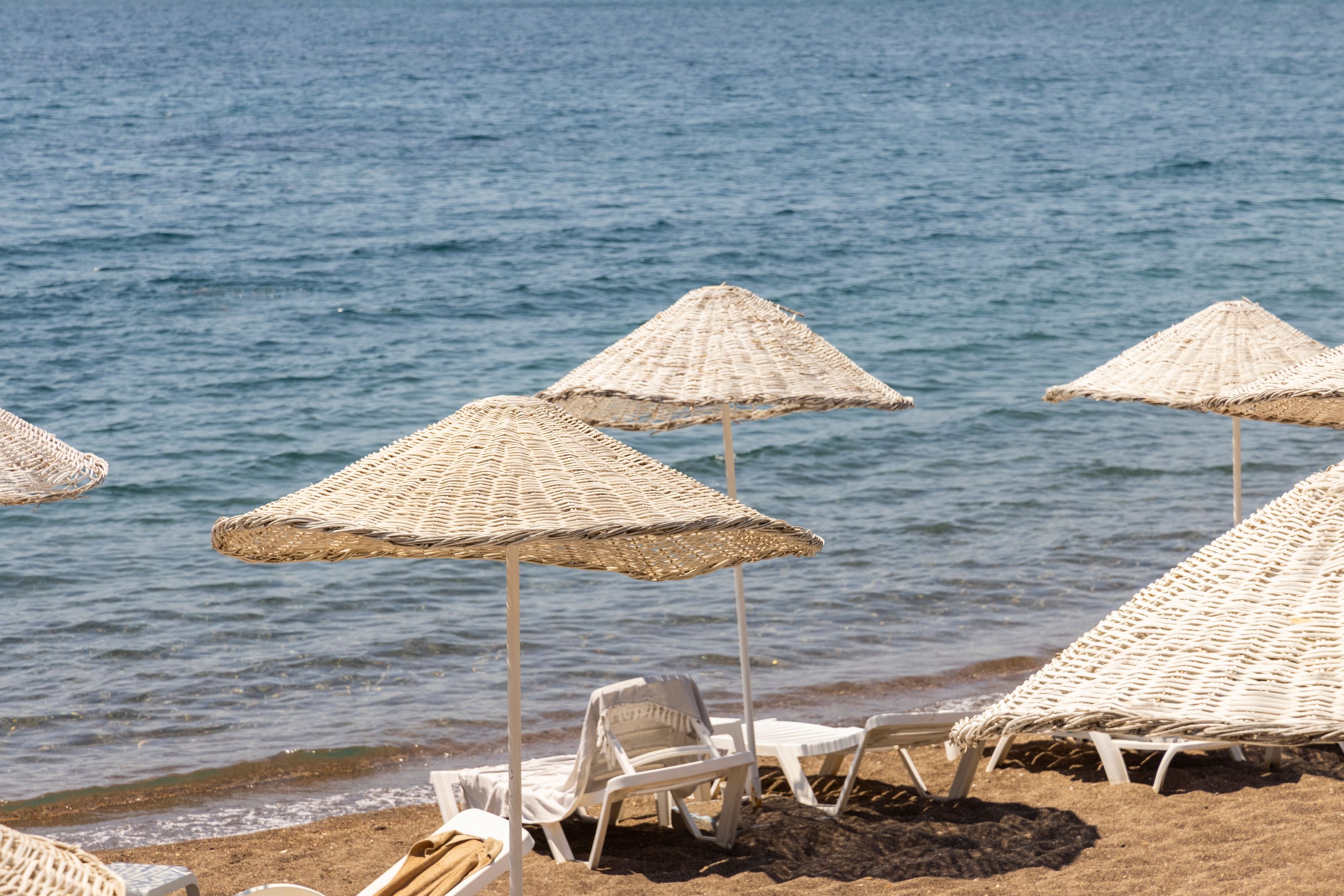 Beach scene with several wicker umbrellas and white lounge chairs near the water.