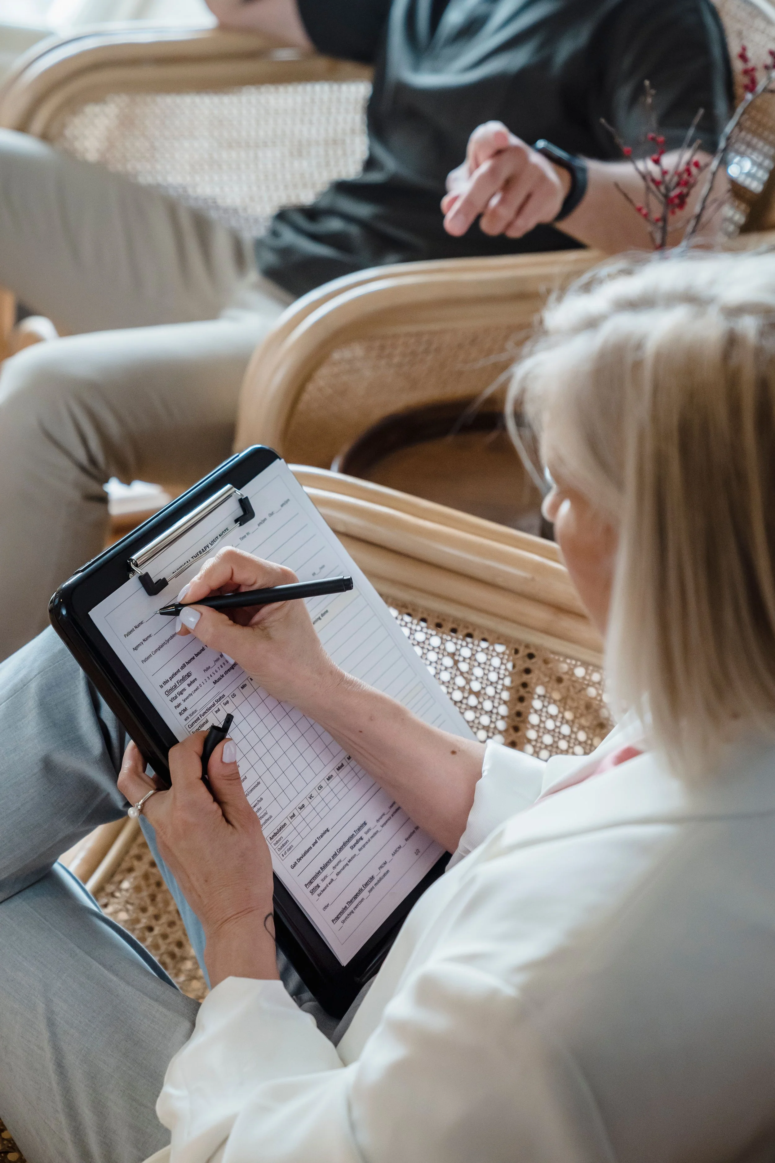 Person in white shirt taking notes on a clipboard during a meeting or conference.