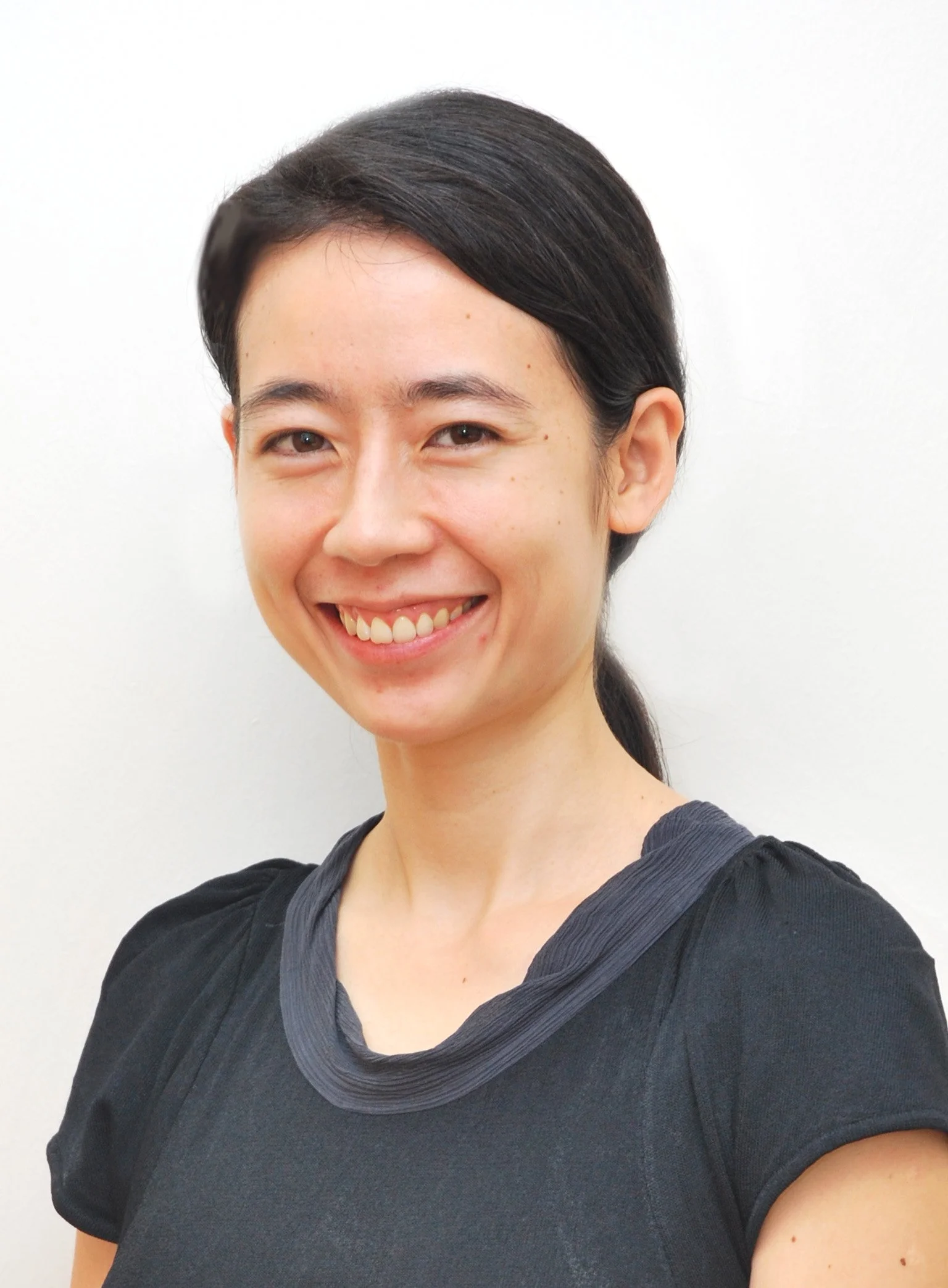 Close-up of a woman with short dark hair, smiling, wearing a black top with a gray scarf.
