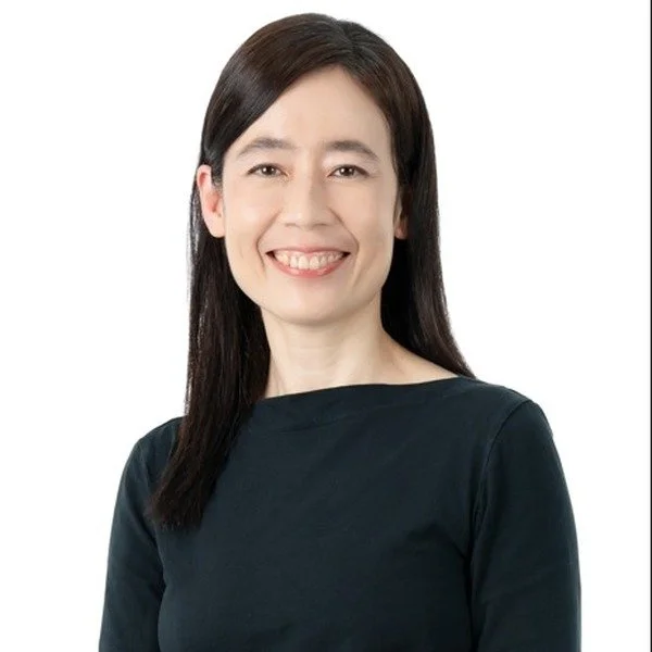 A woman with long dark hair smiling, wearing a dark top, against a white background.