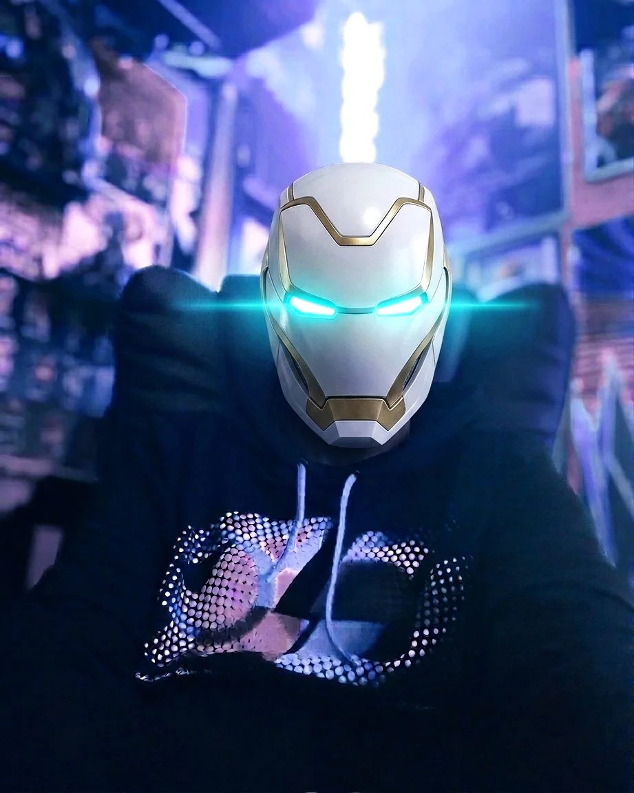 Electronic techno music artist Eternal Surge wearing a futuristic Iron Man like helmet with glowing blue eyes, dark hoodie, in a dimly lit cityscape with neon lights.