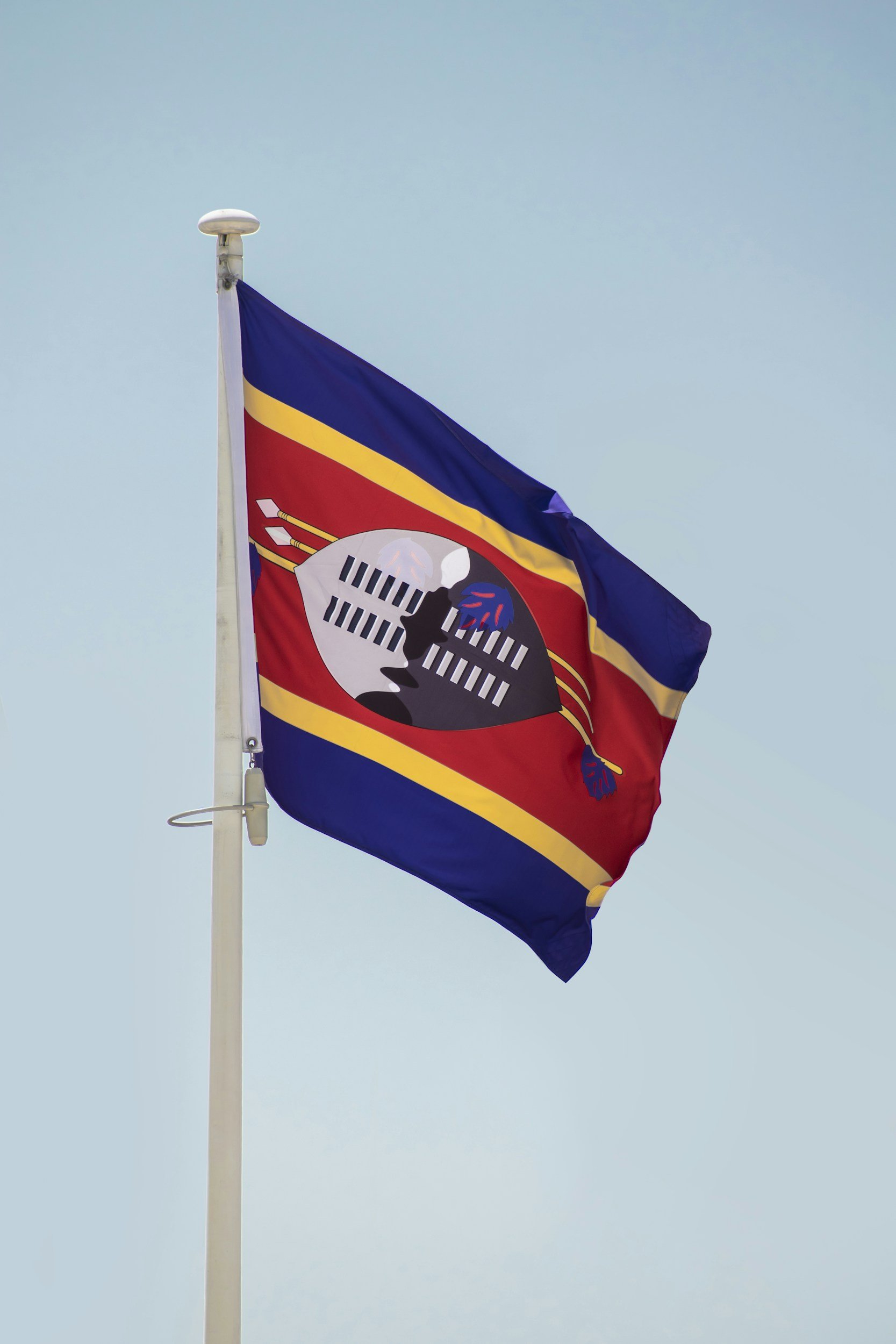 A flag with red, blue, and yellow stripes, featuring a stylized black and white owl with sticks and arrows, flying against a clear blue sky.