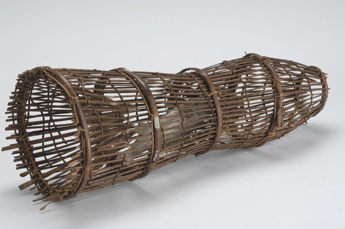A bamboo fish trap with a cylindrical shape and open ends, constructed with horizontal and vertical bamboo slats woven together.