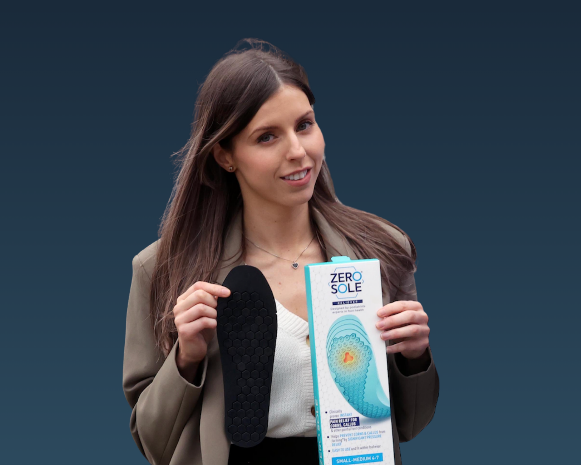 A young woman with long brown hair, wearing a tan blazer and white top, is holding a product brochure titled "Zero Sole" and a black foot pad, while speaking into a microphone at a presentation event against a dark background.