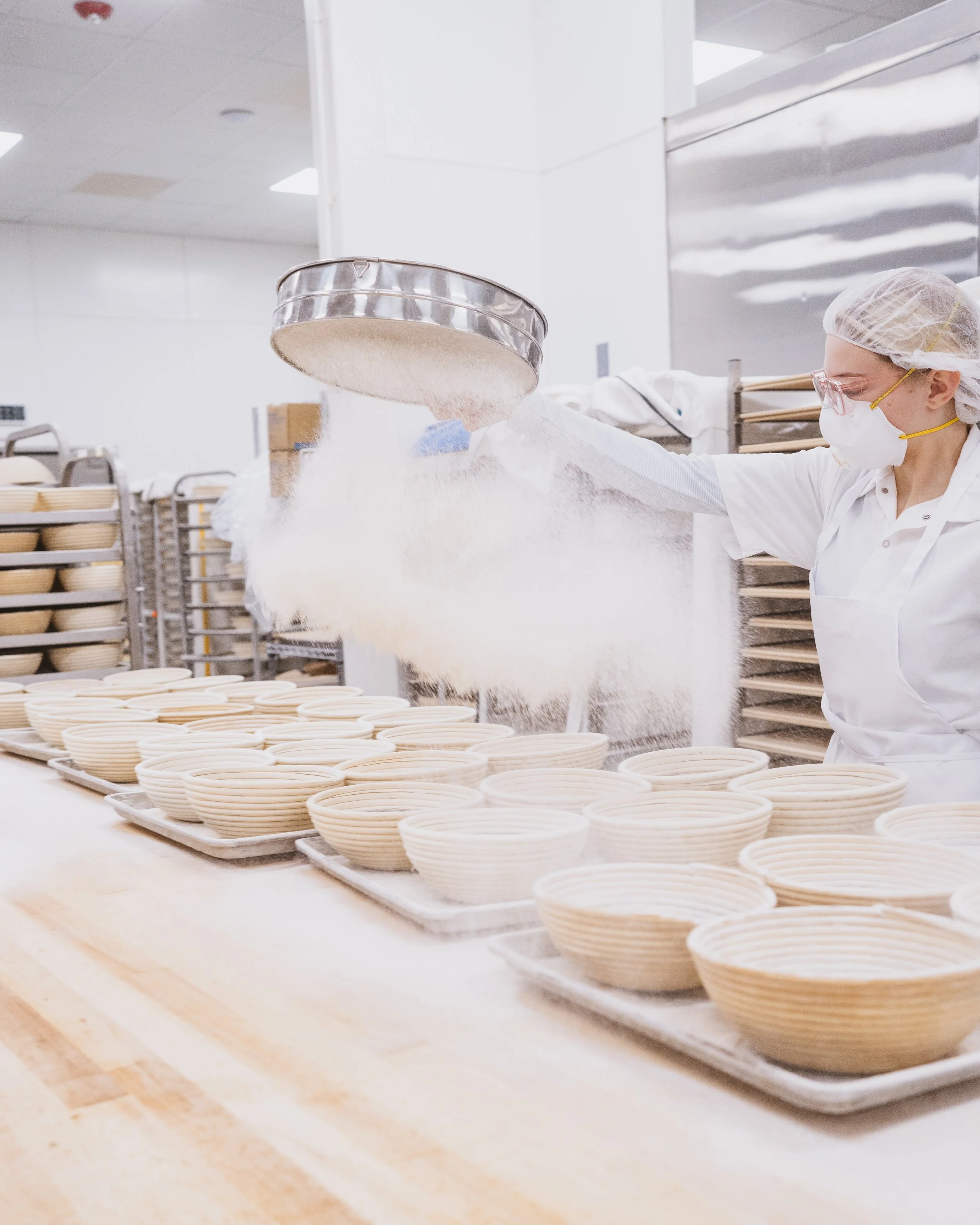 Seven Stars baker dusting flour onto shaping table in the bakery kitchen.