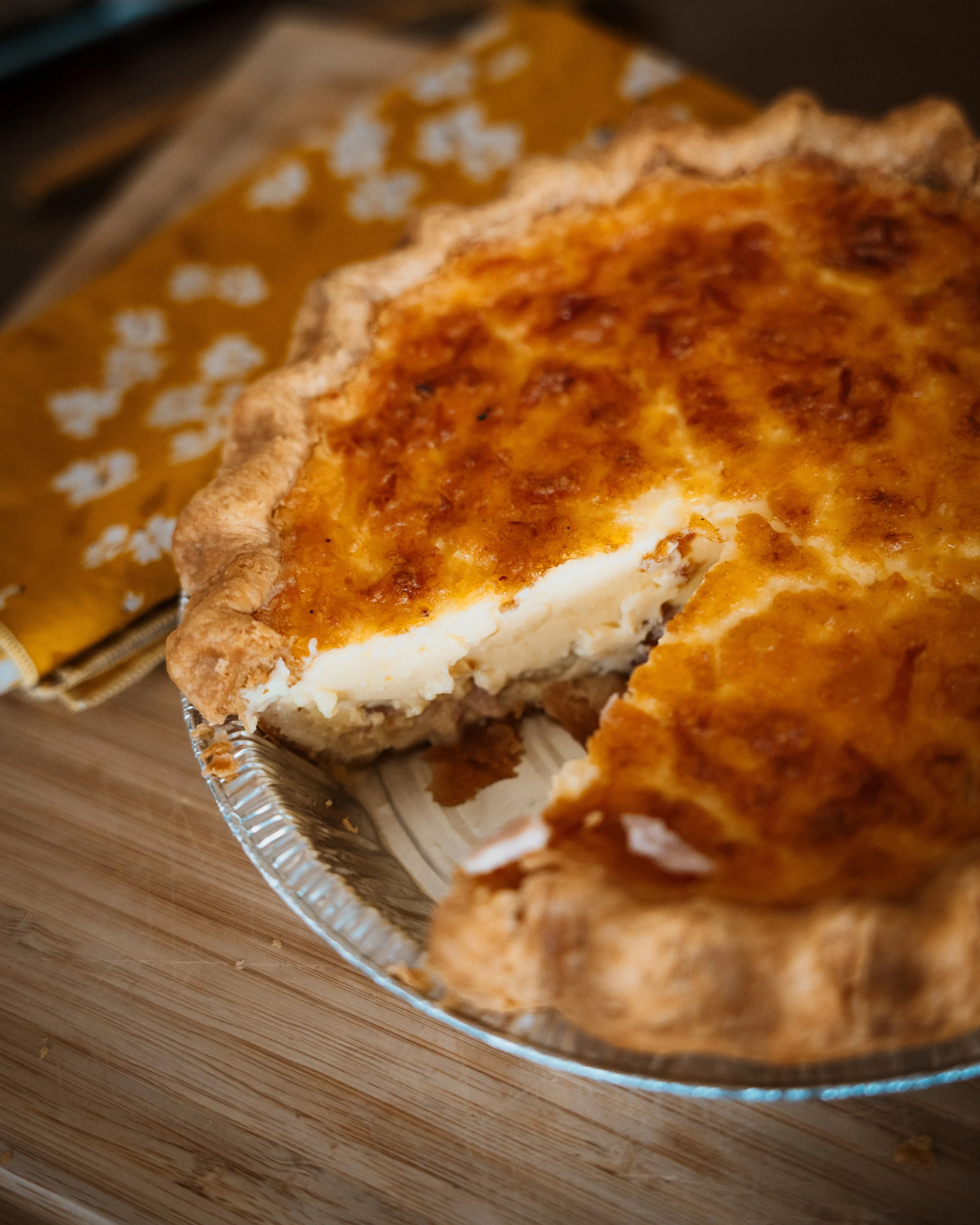 A slice of Seven Stars Bakery quiche with a golden flaky crust in a foil pie tin.