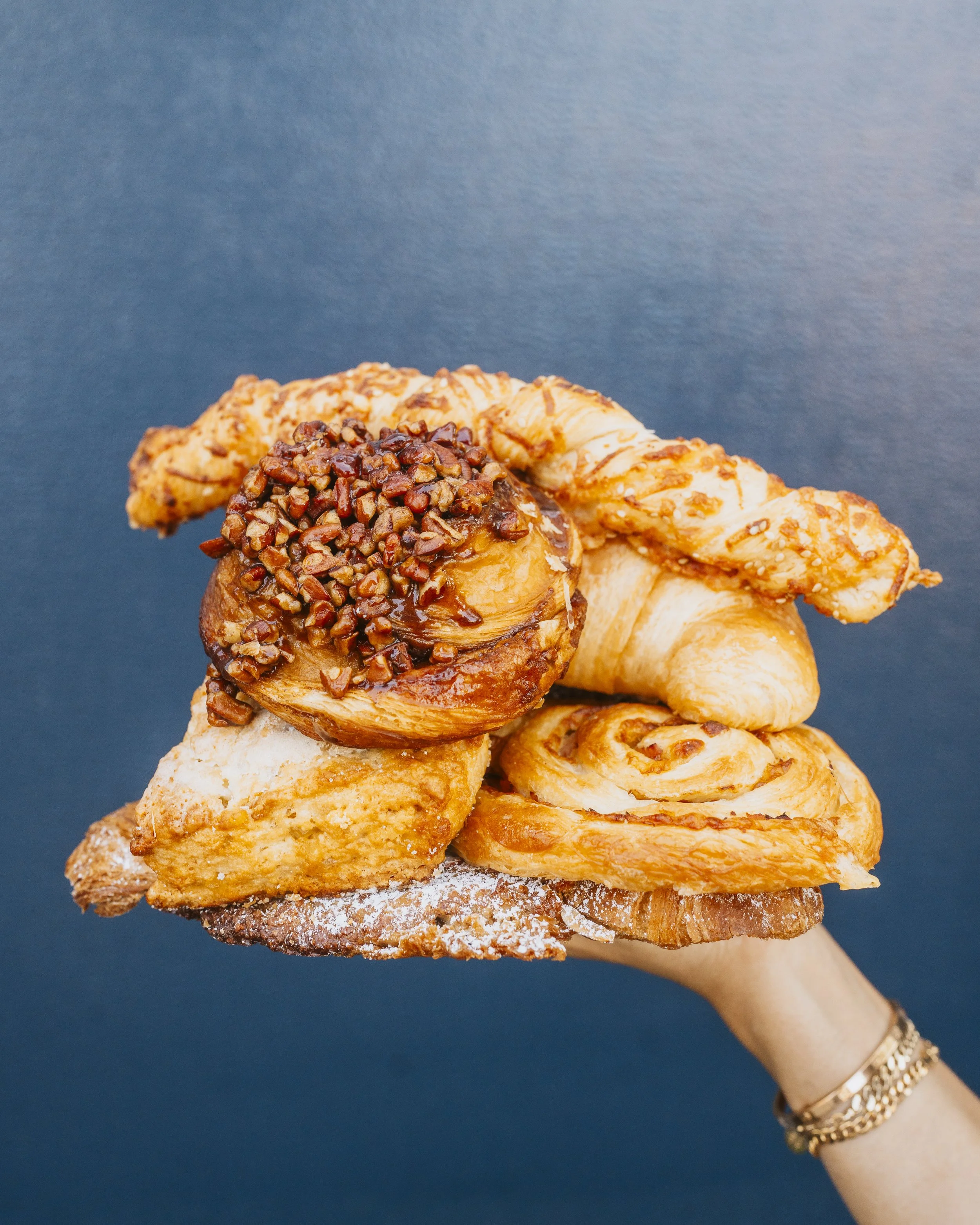 Stack of various flaky pastries and desserts on a hand against a dark background.