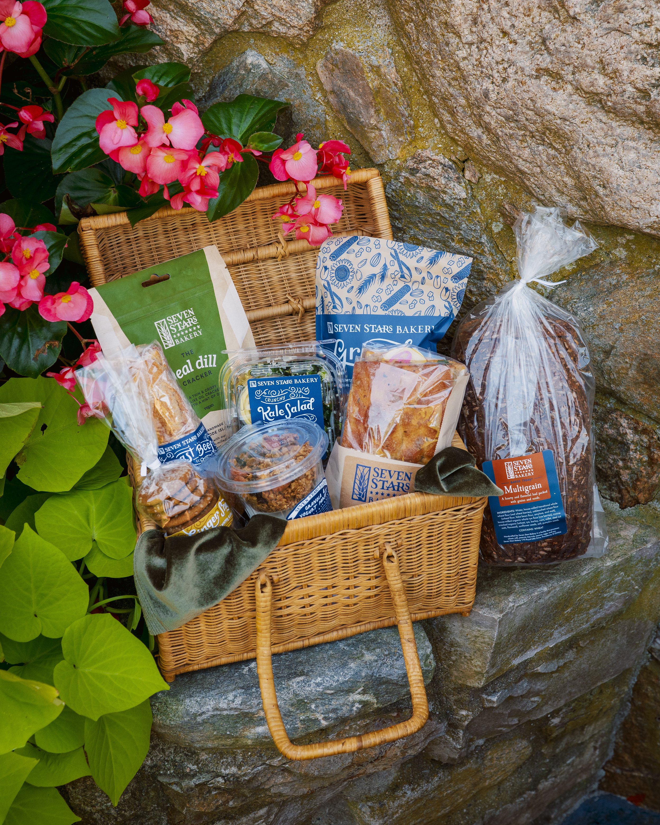 Gift basket of Seven Stars Bakery breads and packaged treats among pink flowers.