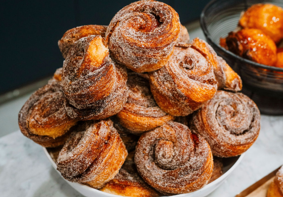 A white bowl filled with cinnamon swirl pastries dusted with powdered sugar.