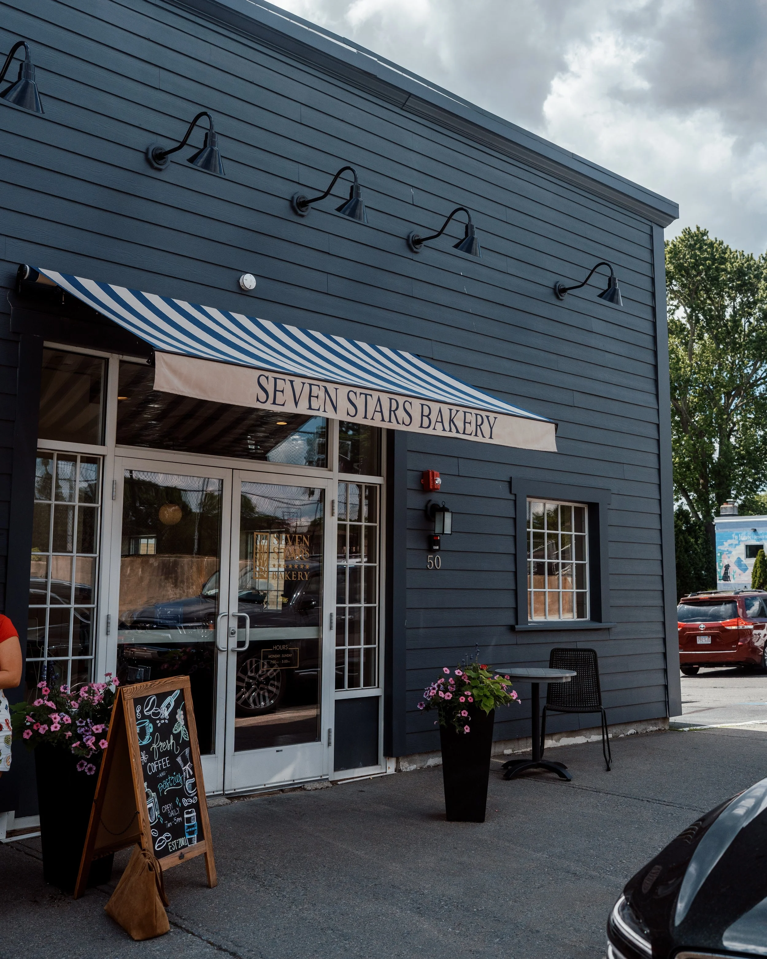 Seven Stars Bakery East Greenwich with a striped awning, pink flowers and outdoor seating.