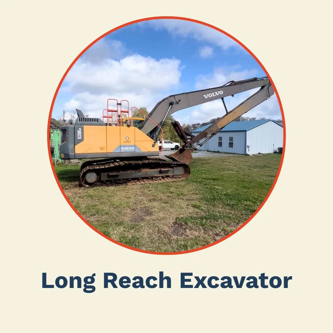 Yellow and gray long reach excavator on grassy area with blue sky and clouds background, next to a blue building.