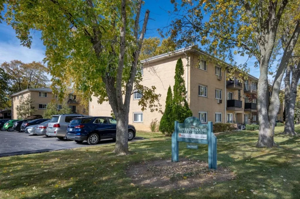 Apartment complex with cars parked in front, trees, and a sign reading Lorraine Court Apartments.