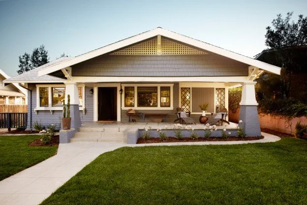 Front view of a single-story house with a porch, white exterior, front steps, and a well-maintained lawn.