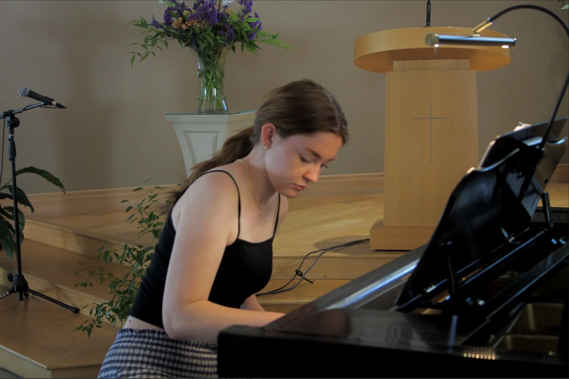 A young woman with red hair is playing a black grand piano, leaning over the keyboard.