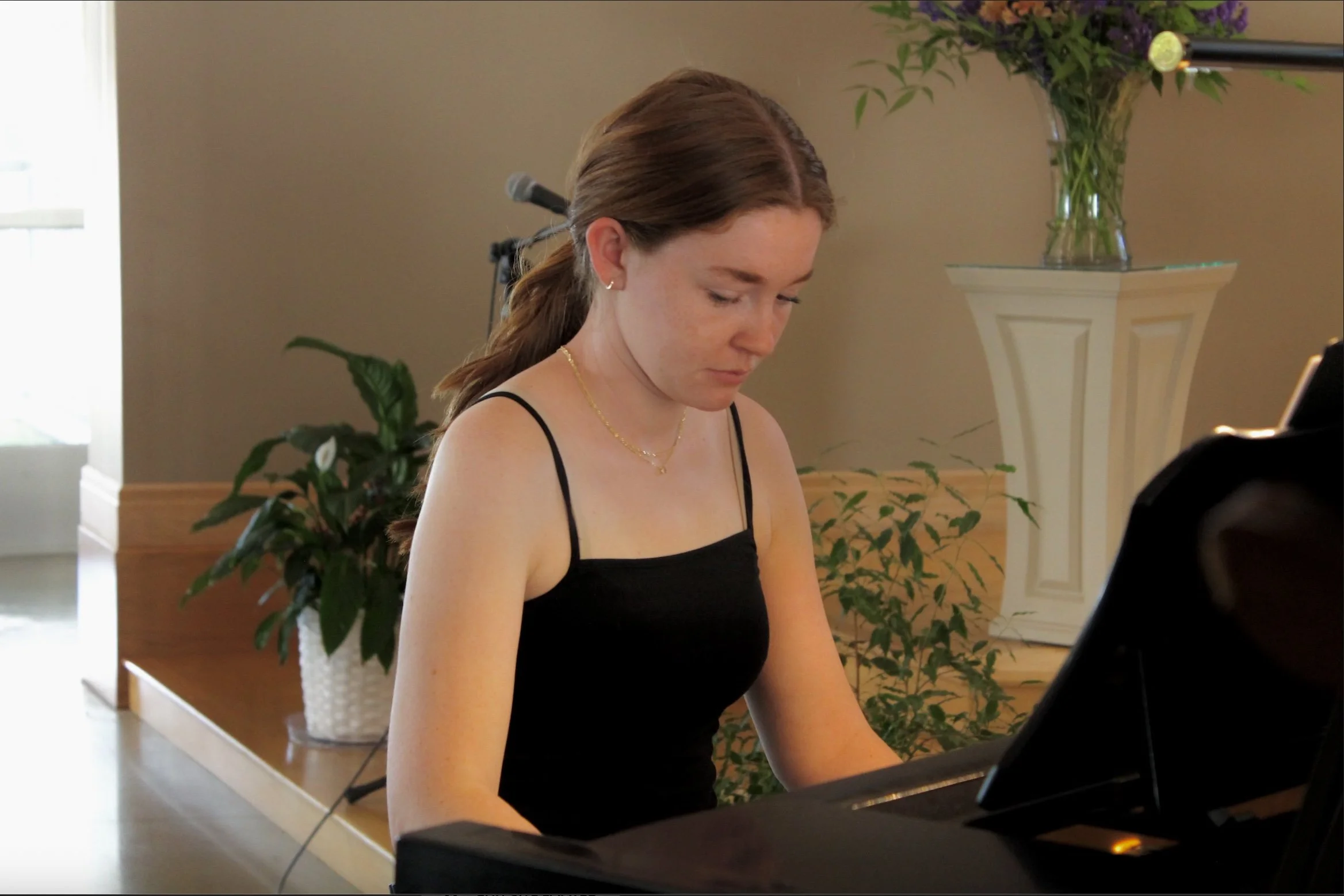 A young woman with red hair is playing a black grand piano.