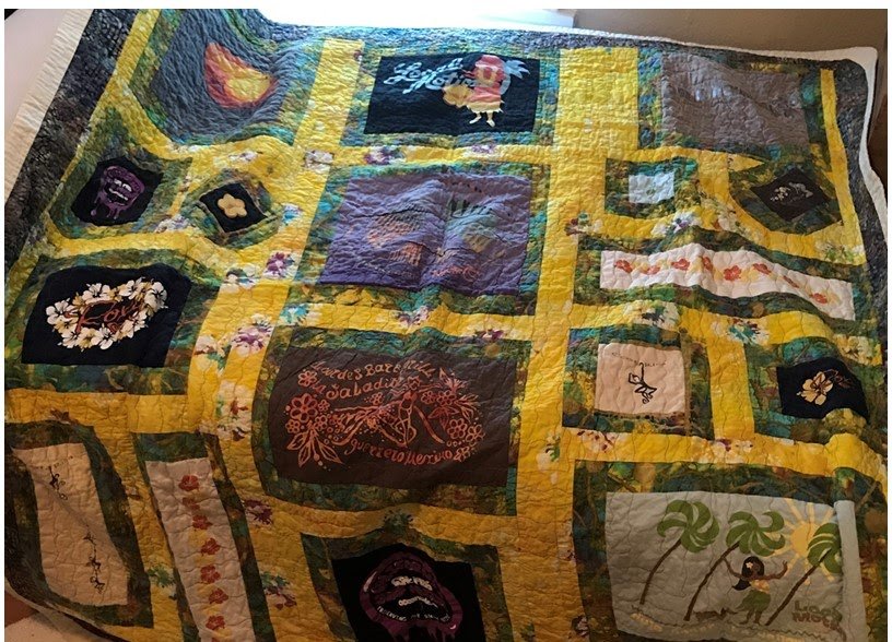 A quilt with various embroidered and appliqued patches featuring floral patterns, text, and images, stitched mainly in yellow, green, and dark backgrounds.