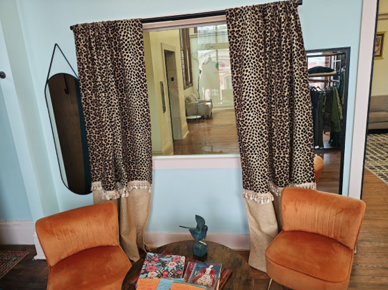 Cozy seating area with two orange velvet chairs, a small round table with magazines, and leopard-print curtains framing a window in a house interior.