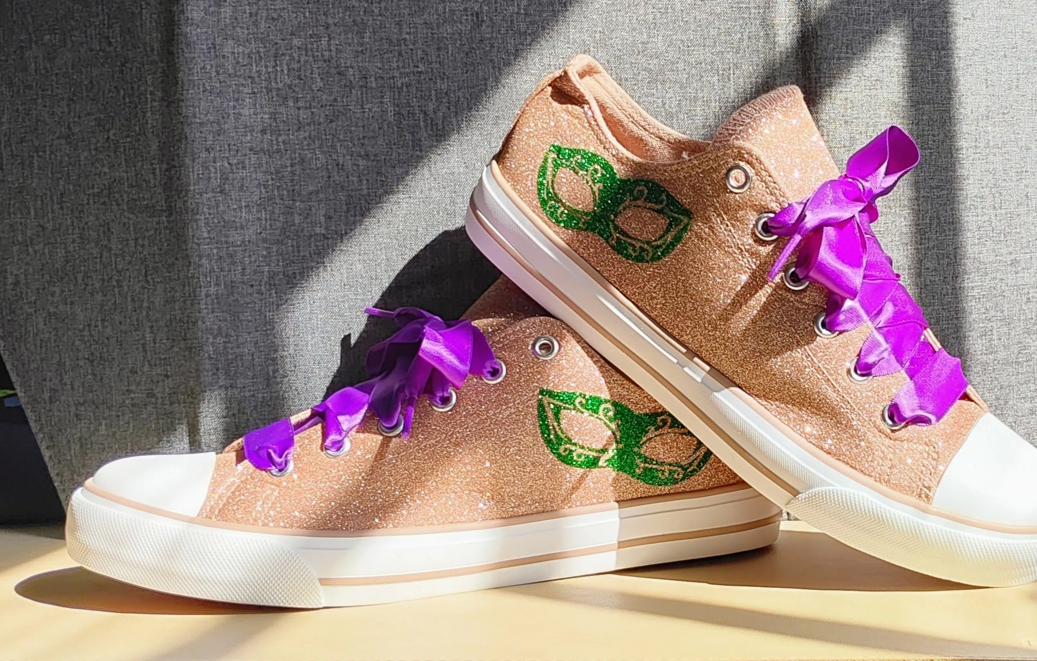 A pair of high-top sneakers with a glittery pink surface and purple laces. The sneakers feature a green design on the sides and have a white sole with a textured bottom.