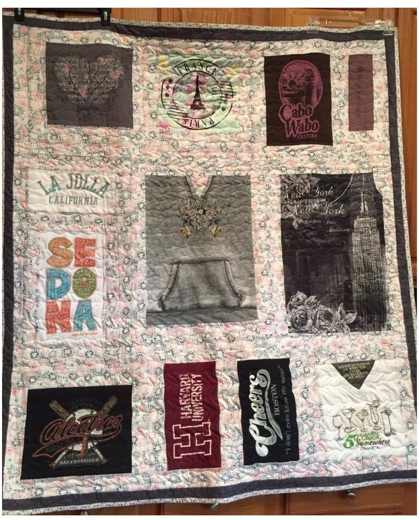A quilt featuring various university logos and designs, including UCLA, Texas A&M, and the University of California. The quilt has a patterned background and a dark border.