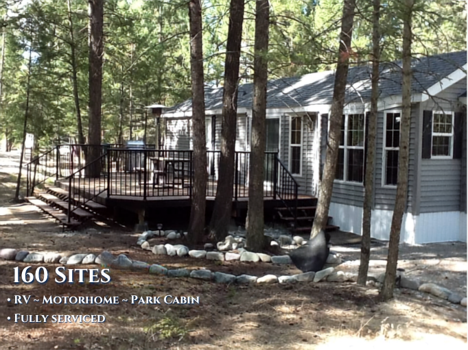 A gray house with a deck in a wooded area, surrounded by trees and rocks
