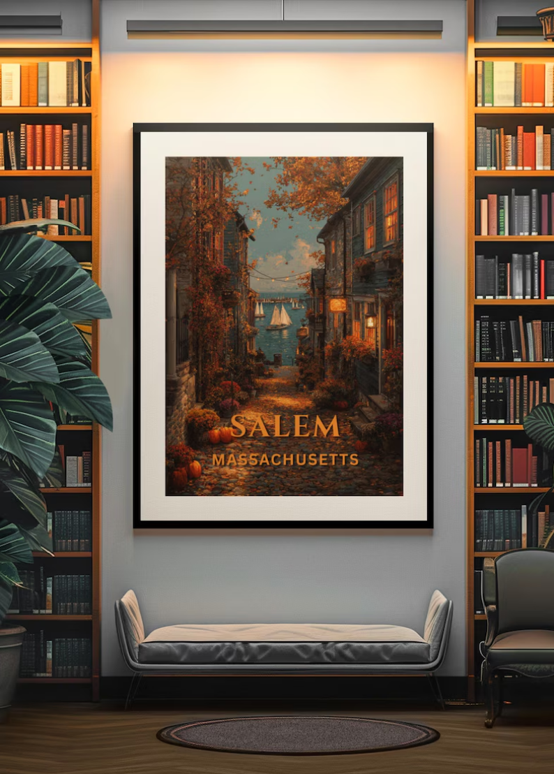 A framed poster of Salem, Massachusetts, with a street scene leading to the water, autumn leaves, and sailboats, hung on a wall between two bookshelves, with a bench and chair below.