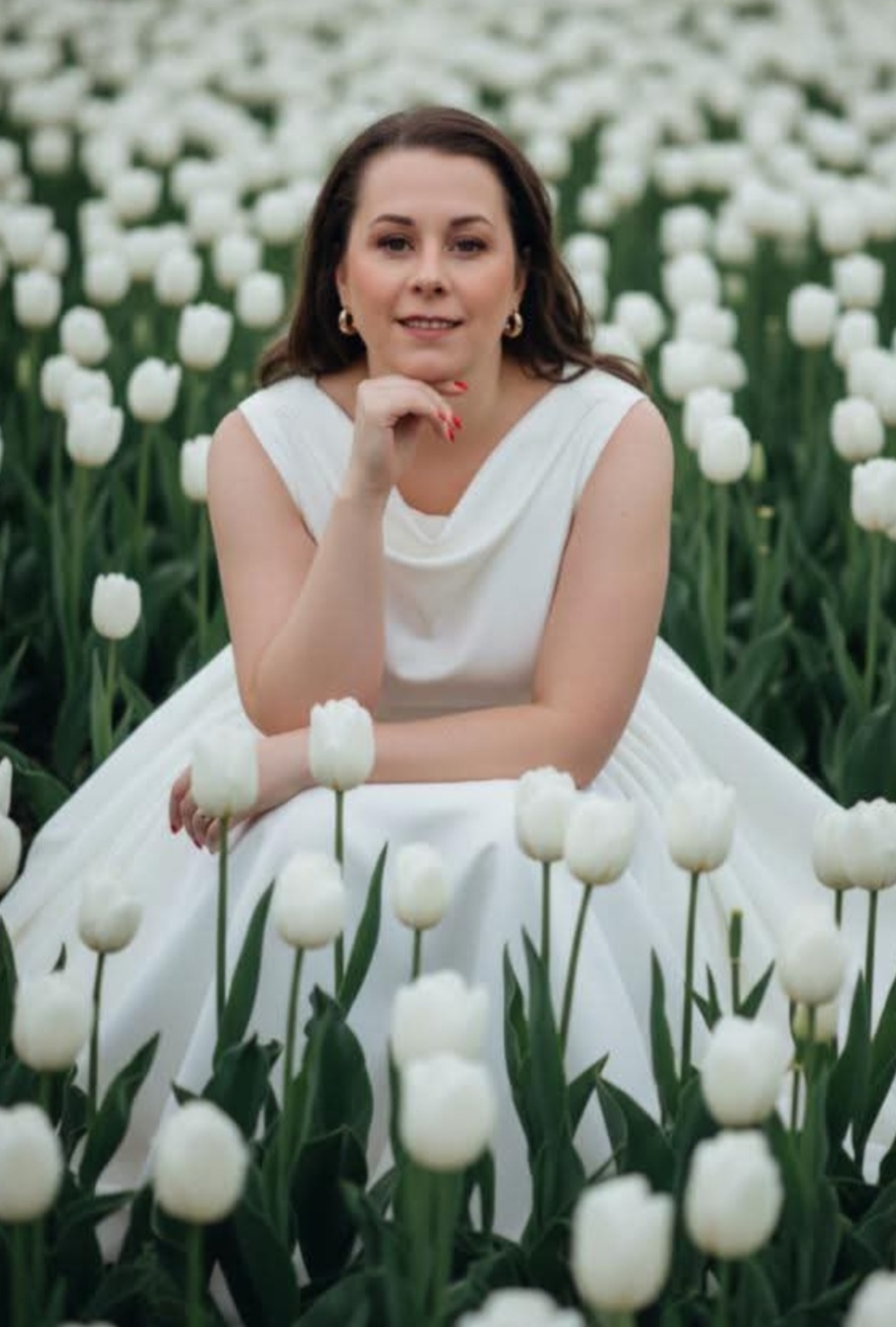 A woman in a white dress sitting in a field of white tulips.