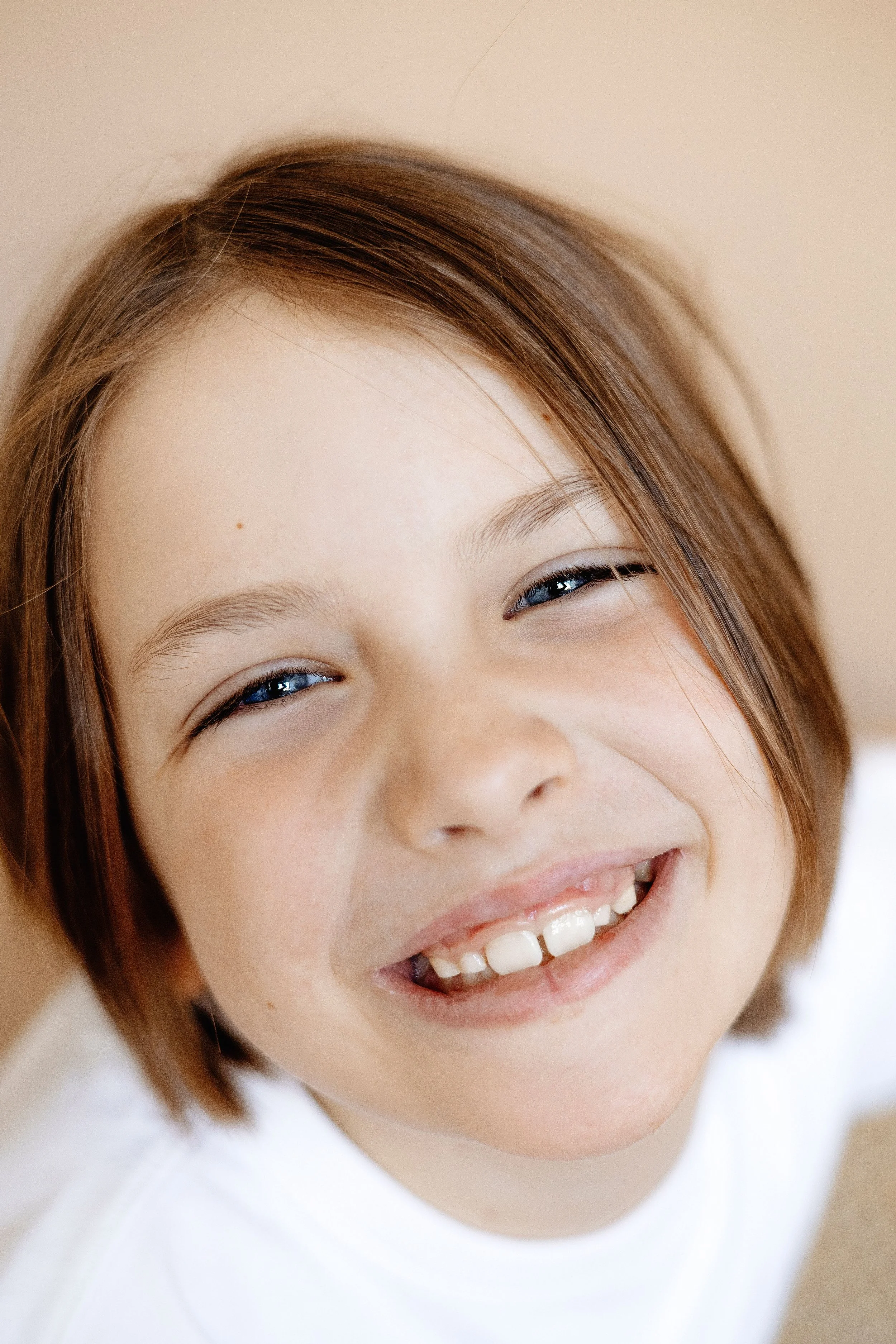 Close-up of a young woman's face showing her smiling with visible blue eyes, light skin, and brown hair styled in a casual manner.