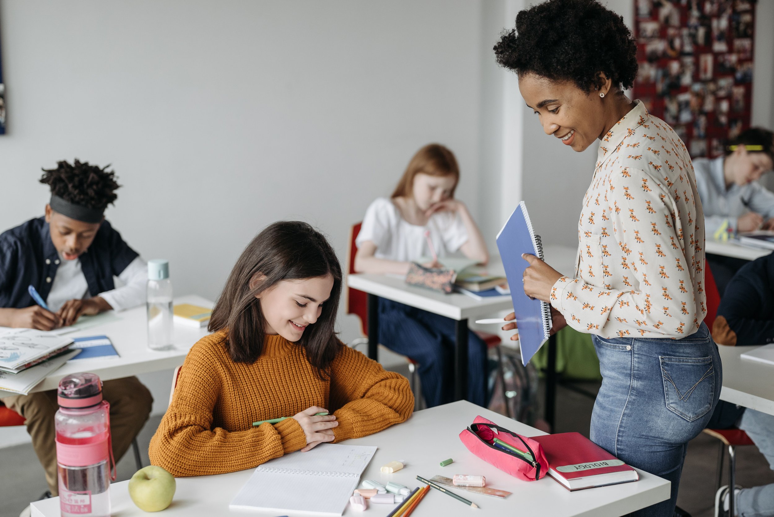 A teacher talking to students in a classroom with students working at desks.