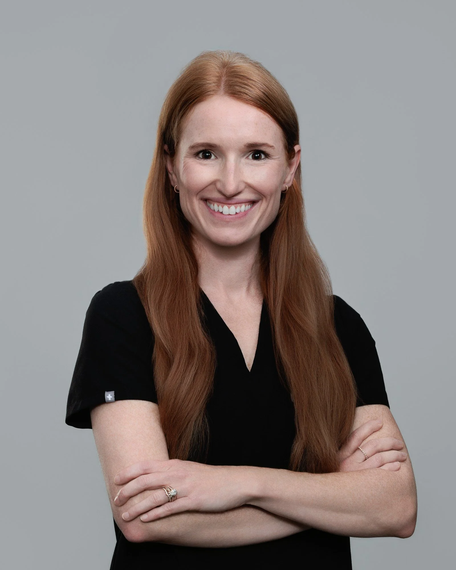 A woman with long hair wearing a black shirt, standing against a neutral background.