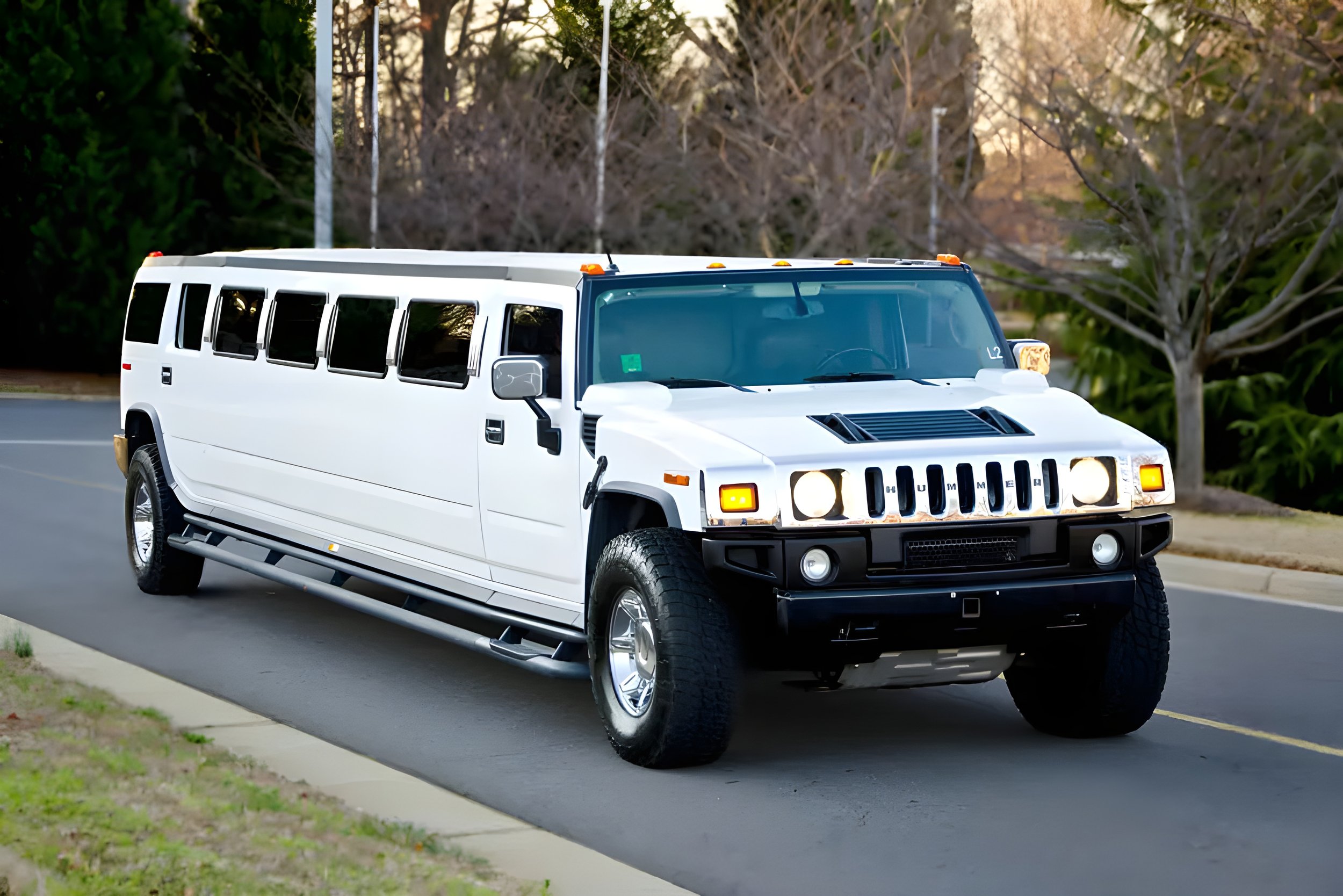 A white Hummer H2 SUV driving on a residential street with trees in the background.