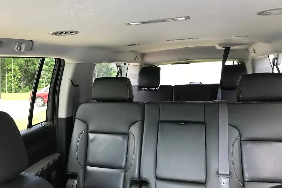 Interior of a SUV with black leather seats, three rows of seats, and a window showing a red car and greenery outside.