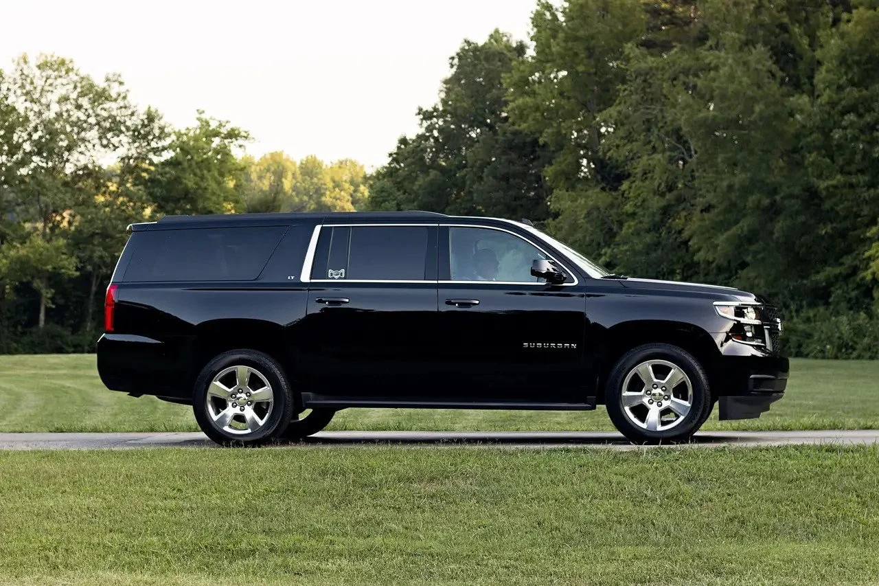 A black Chevrolet Suburban SUV parked on a grassy area with trees in the background.
