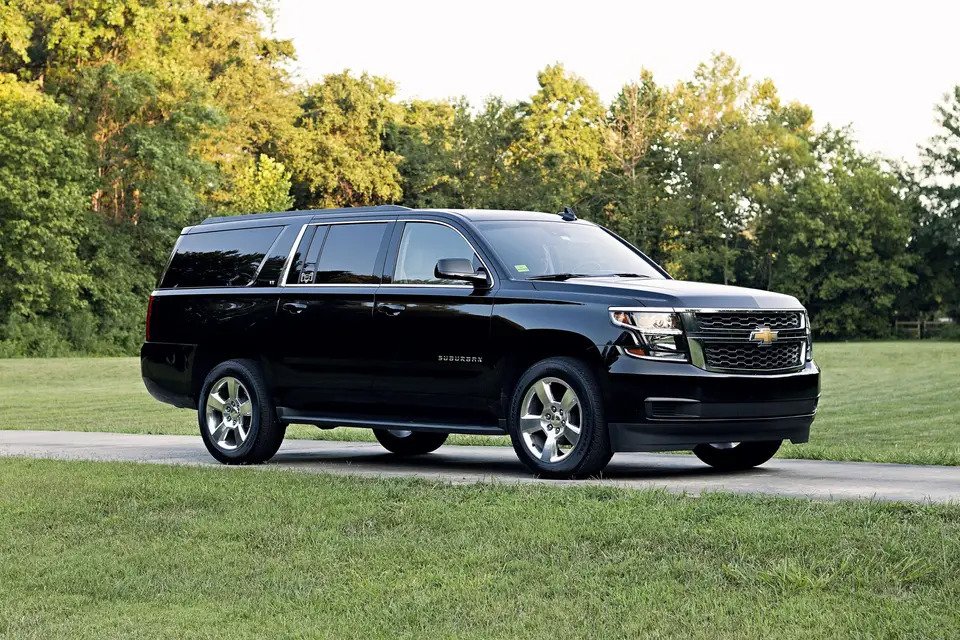 Black Chevrolet Suburban parked on a driveway with trees and grass in the background.