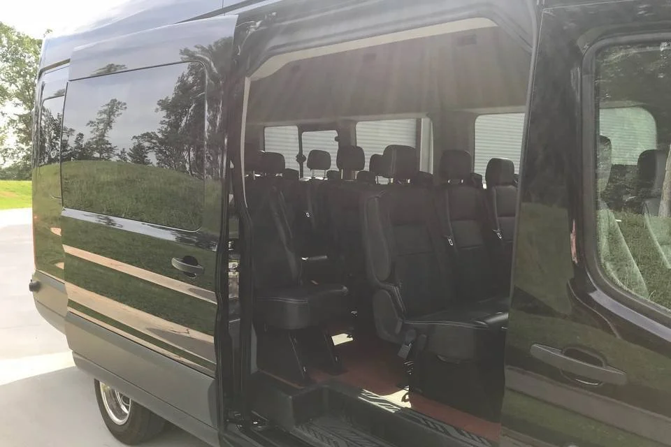 Black passenger van with open sliding door, showing multiple rows of black seats inside, parked outdoors on a sunny day.