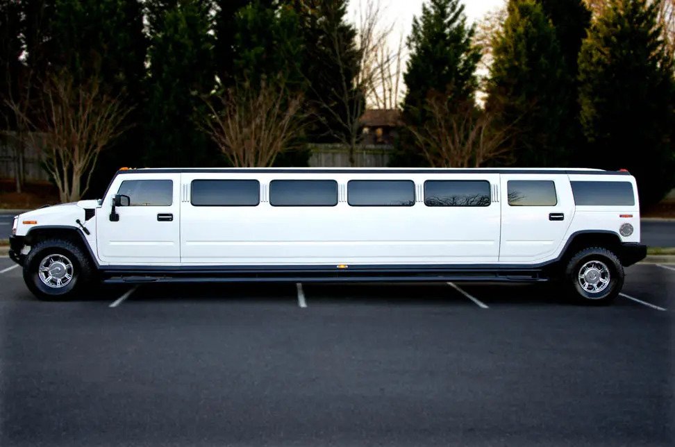 White stretch limousine parked in an empty parking lot with trees in the background.