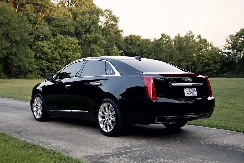 Black Cadillac sedan parked on a concrete driveway in a grassy area with trees in the background.